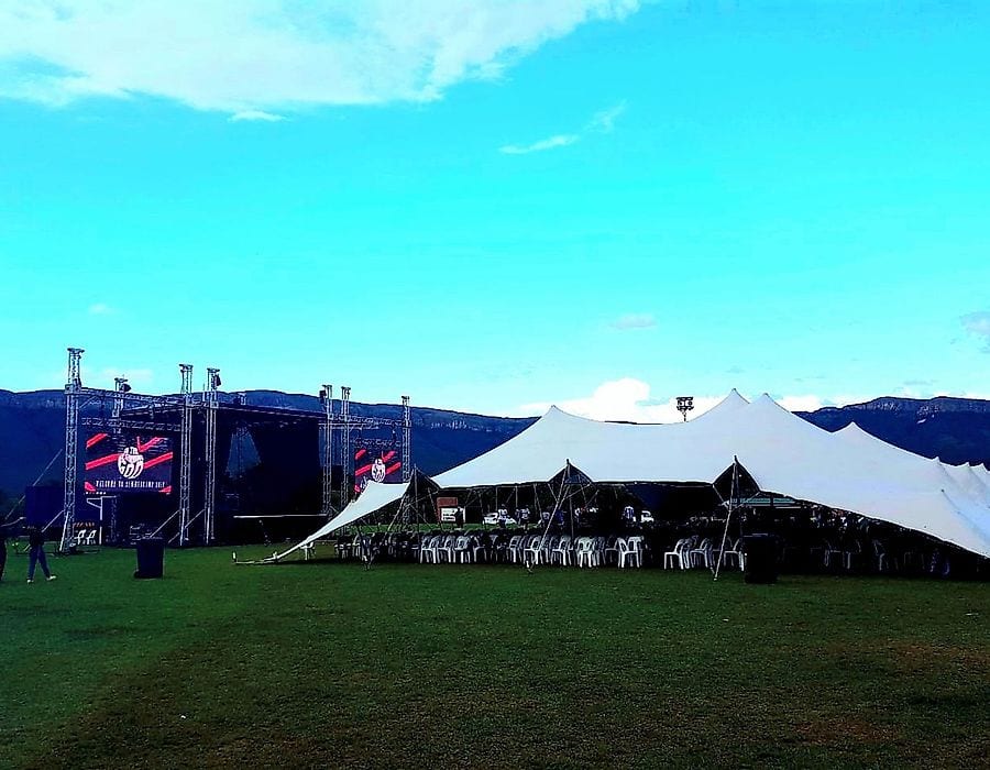 White stretch tents beside a stage truss on a lawn