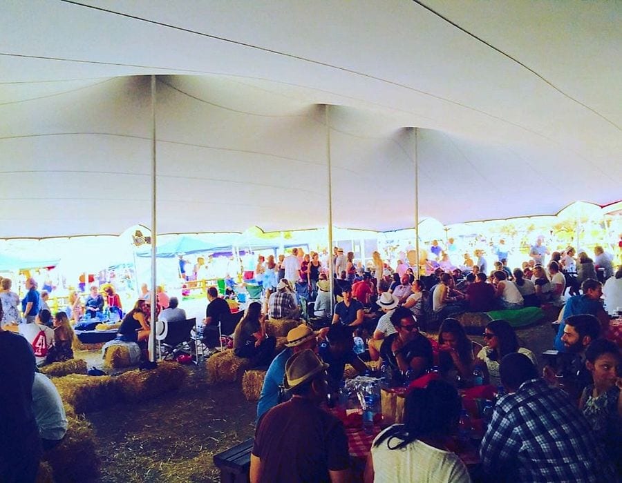 A festival crowd under a large white stretch tent