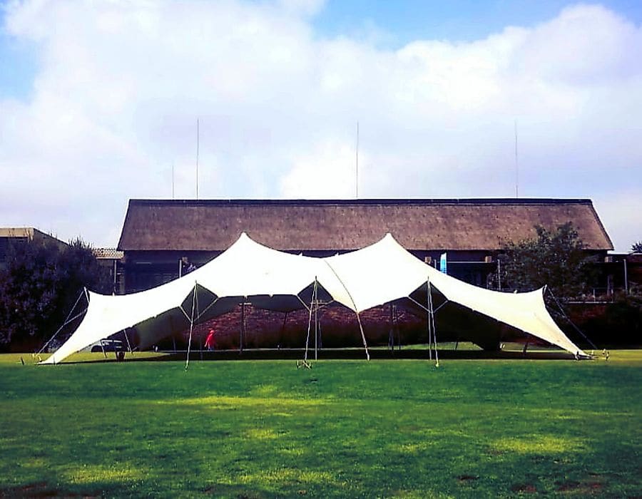 A white stretch tent on a lawn in front of a thatched venue